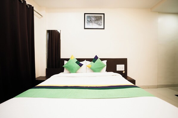 A neatly made bed with a green and purple striped bedspread, a white headboard, and two pillows with geometric patterns. - Kaizen Stays & Resto (Wai)