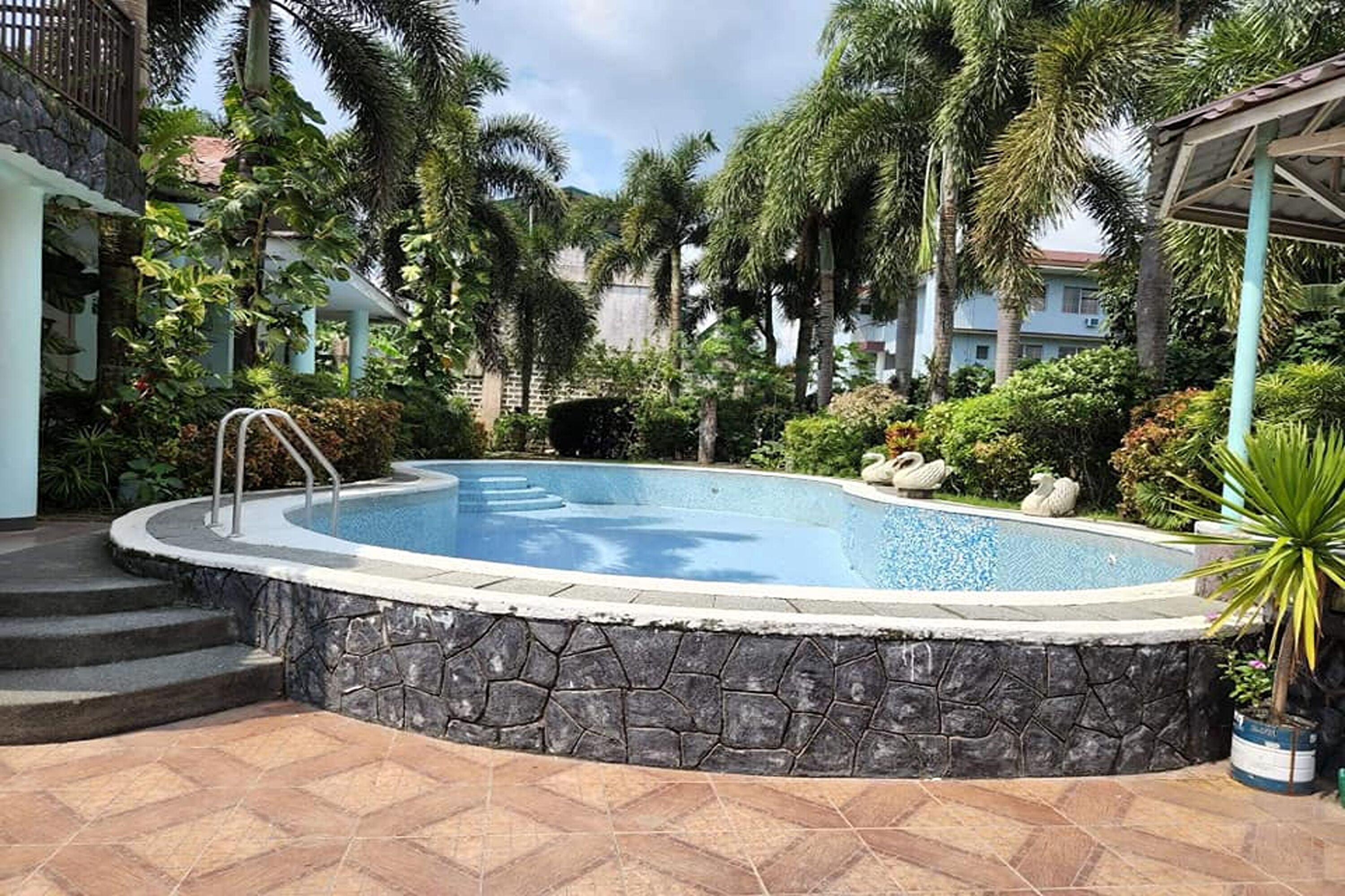 A swimming pool surrounded by stone walls, palm trees, and a gazebo.