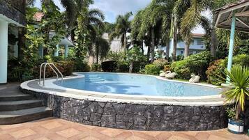 A swimming pool surrounded by stone walls, palm trees, and a gazebo.