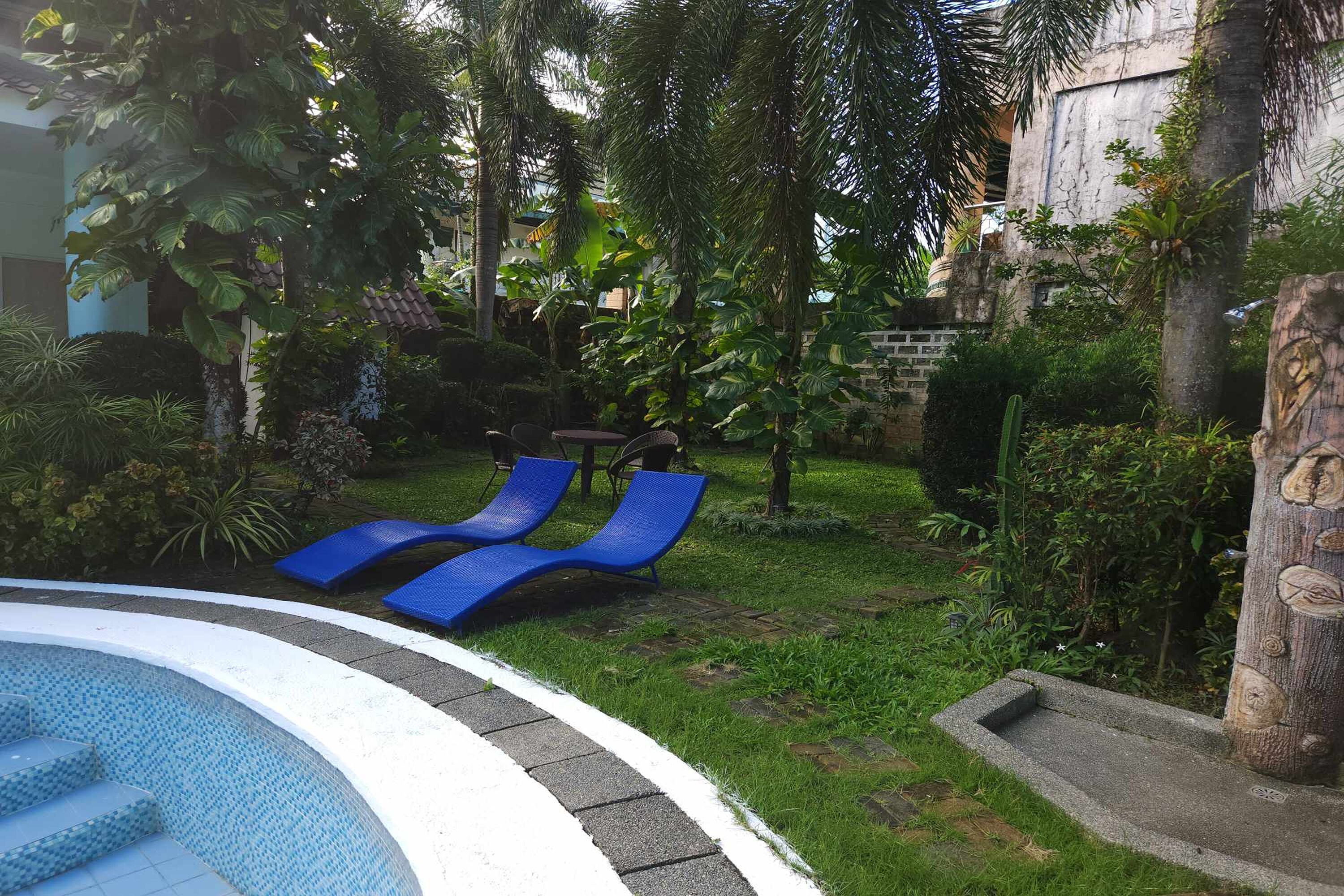 A pool area with blue lounge chairs, surrounded by lush greenery and a stone wall.