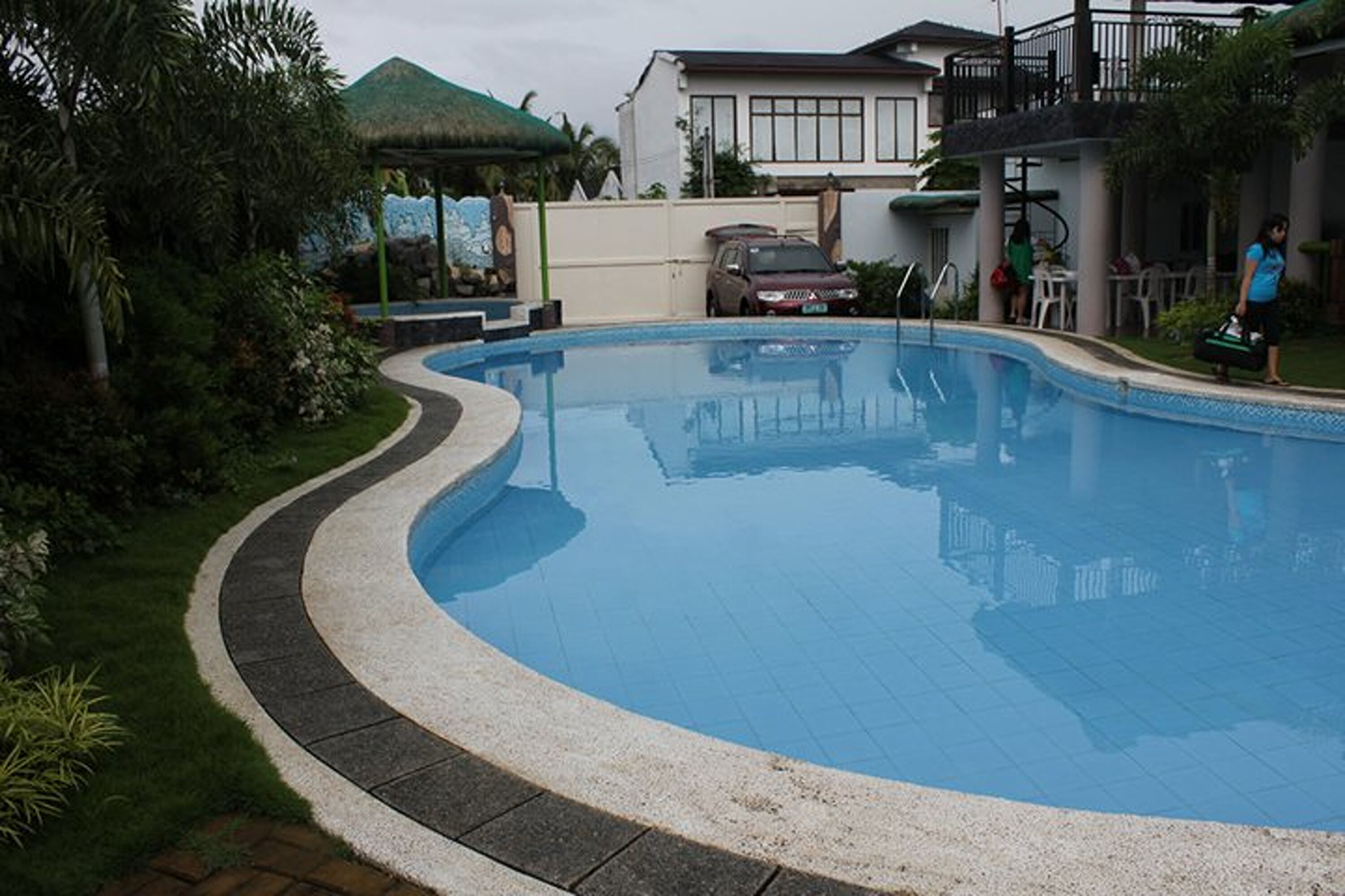 Una piscina de borde curvo, rodeada por un solado empedrado y abundante vegetación.