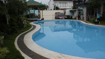Una piscina de borde curvo, rodeada por un solado empedrado y abundante vegetación.