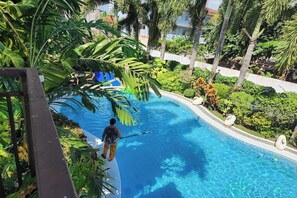 A pool area with a person cleaning it, surrounded by lush greenery and palm trees. - Villa Celine Bay Laguna (Bay)
