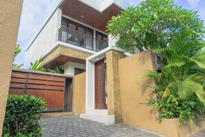 A modern two-story house with a balcony, a wooden gate, and lush greenery. - Miles Villa (Nusa Dua)