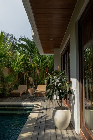 A wooden deck with a pool, surrounded by lush tropical plants and wicker furniture. - Miles Villa (Nusa Dua)