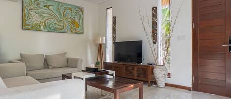 Una sala de estar moderna con sofá, mesa de centro, televisor y elementos decorativos.