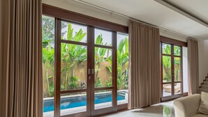 A room with large windows, a pool, and a beige sofa. - Miles Villa (Nusa Dua)