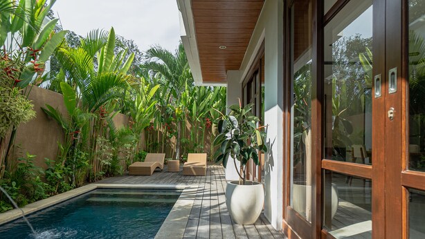 A poolside area with a wooden deck, lounge chairs, and lush tropical plants. - Miles Villa (Nusa Dua)