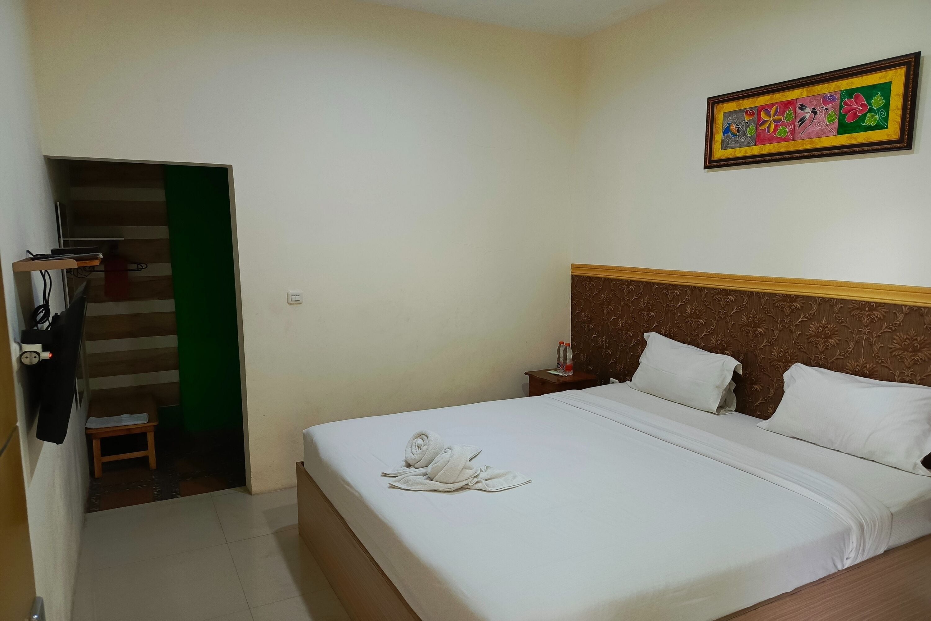 Una habitación de hotel con cama, mesita de noche, un cuadro, una puerta verde y un taburete pequeño.