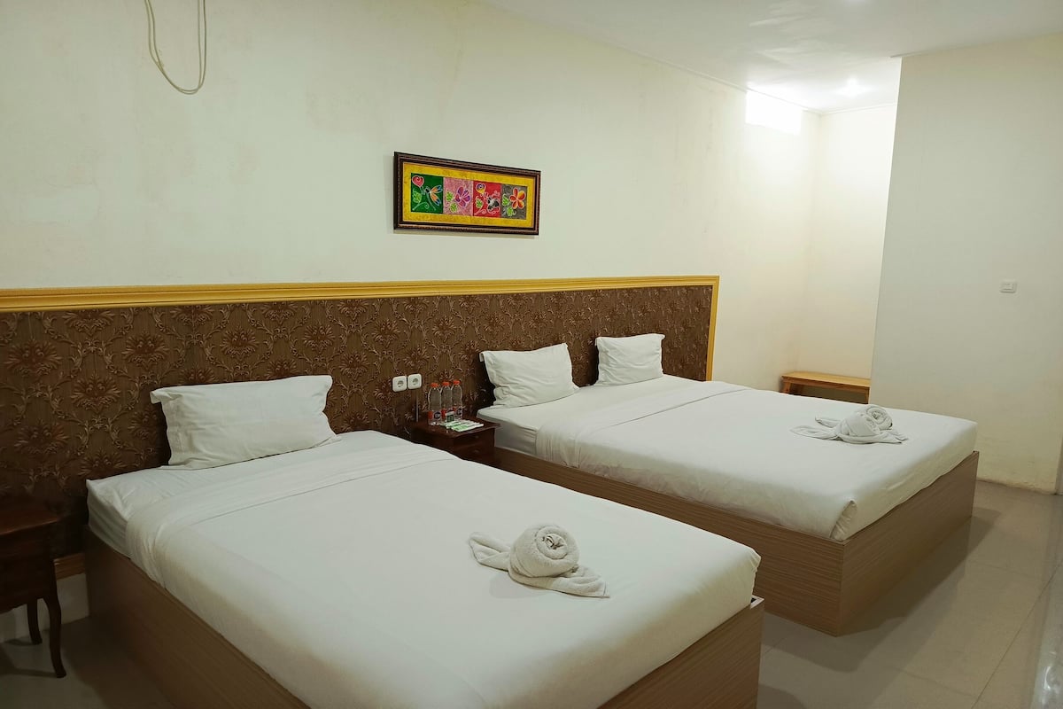 A hotel room with two beds, a wooden headboard, a framed artwork on the wall, and a neatly made bed with a towel.