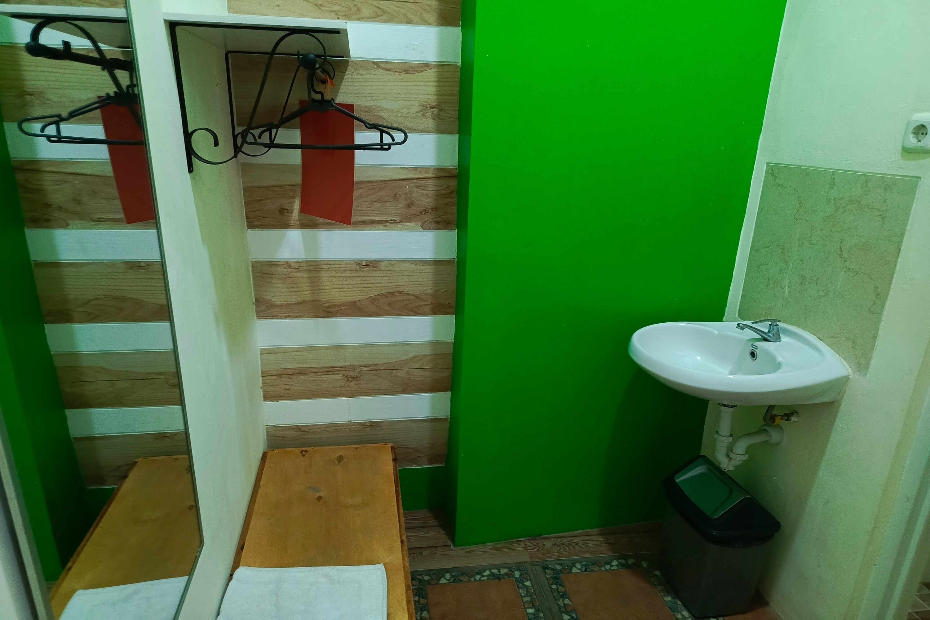 A bathroom with a wooden bench, a sink, and a trash bin.
