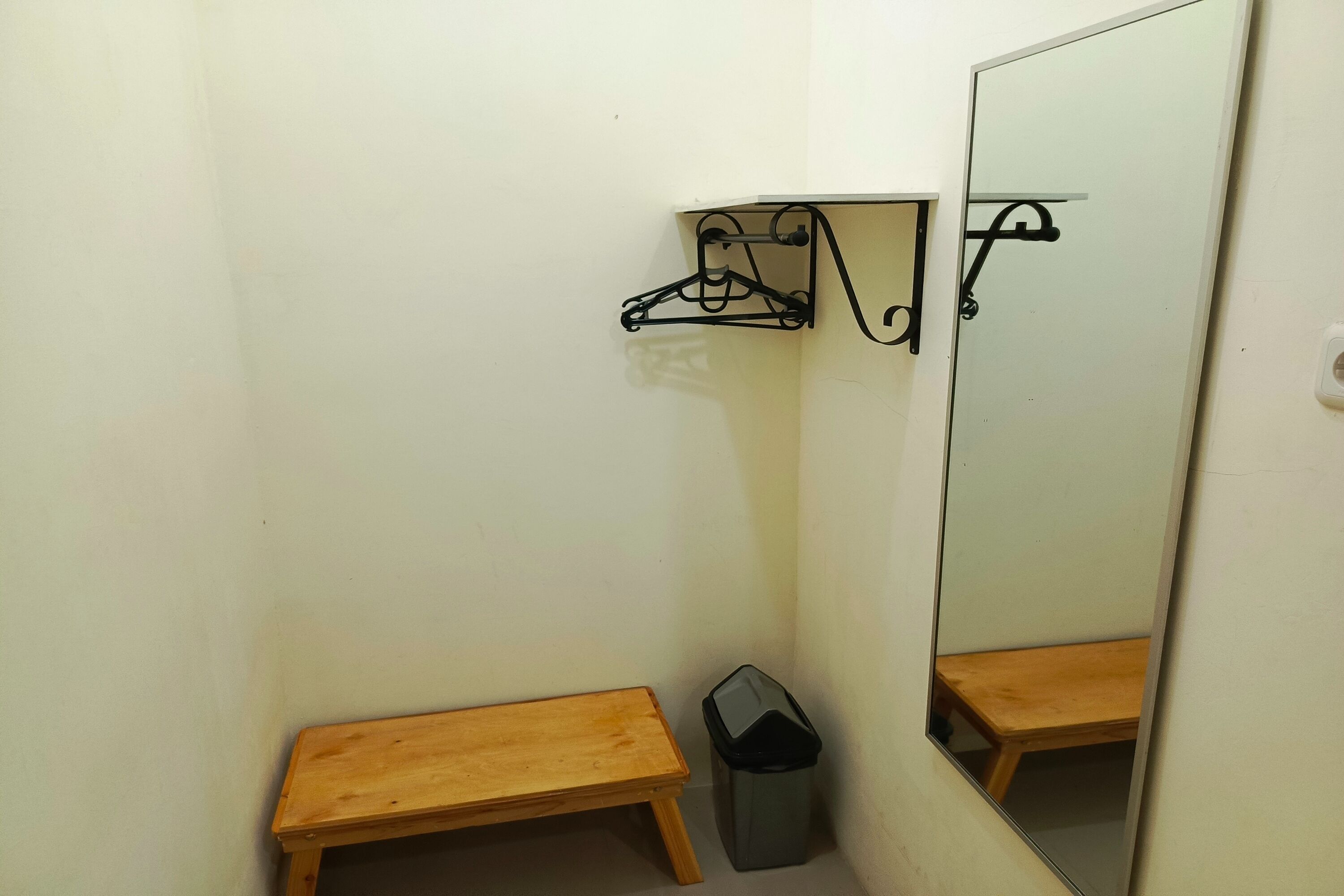 A small bathroom with a wooden bench, a trash bin, and a mirror.