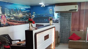 A reception area with a modern desk, a cityscape mural, and a sofa with a red pillow. - Hotel Alexa (Ahmedabad)