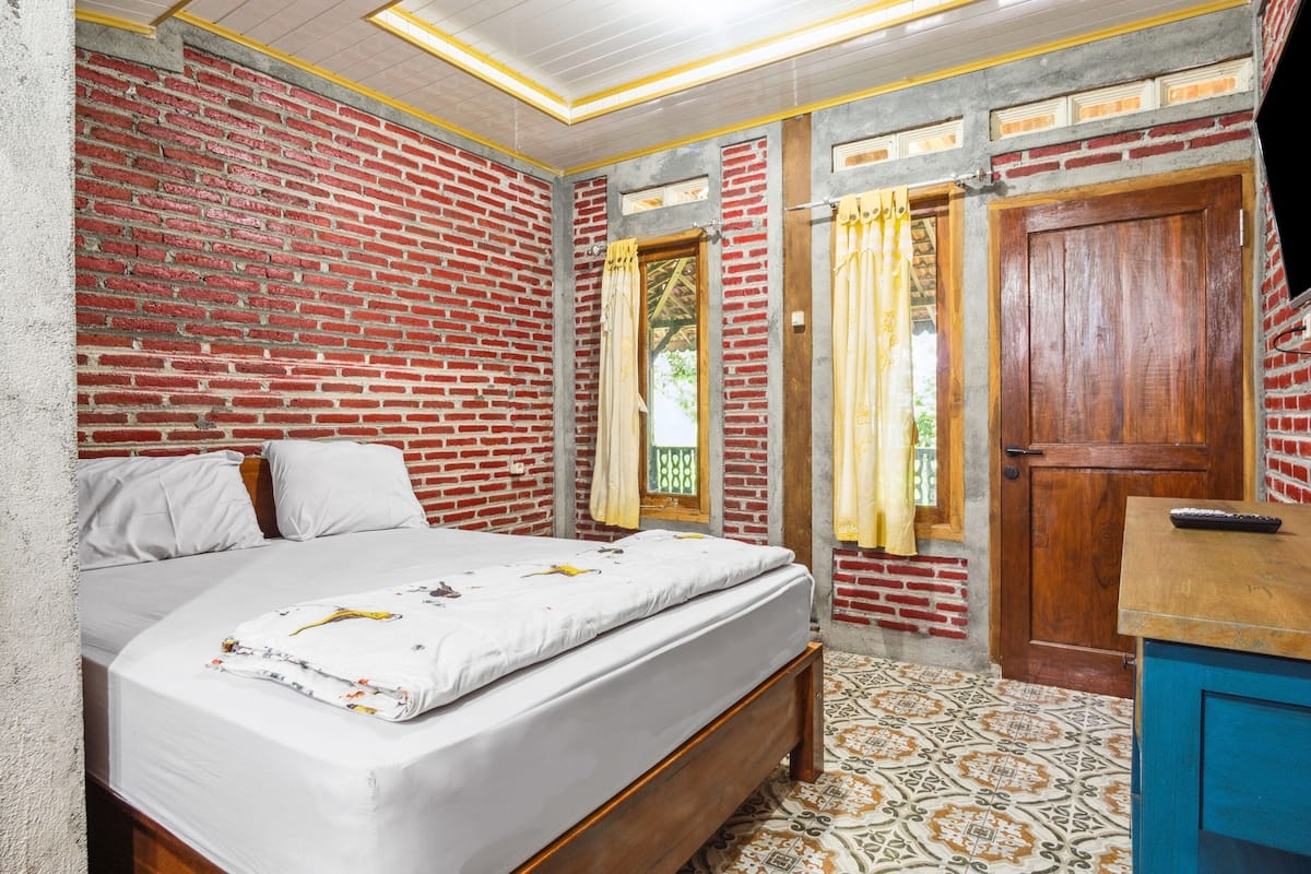 Une chambre avec un mur en briques, un lit en bois, une armoire bleue et des carreaux de sol à motifs.