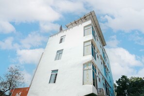 Een meerlaags gebouw met een witte gevel en blauwe accenten, met meerdere ramen en een zichtbaar bord.