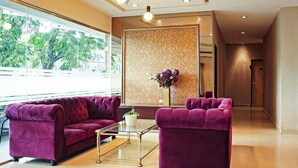 Un hall d’entrée moderne avec un ensemble de canapés violets, une table basse en verre et une plante décorative.