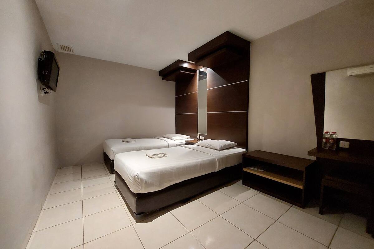 Ein Hotelzimmer mit zwei Betten, einem kleinen Schreibtisch, einem Spiegel und einer Bank.