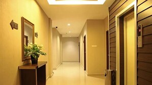 Un couloir d’hôtel avec un miroir, une plante en pot, un ascenseur et une poubelle.