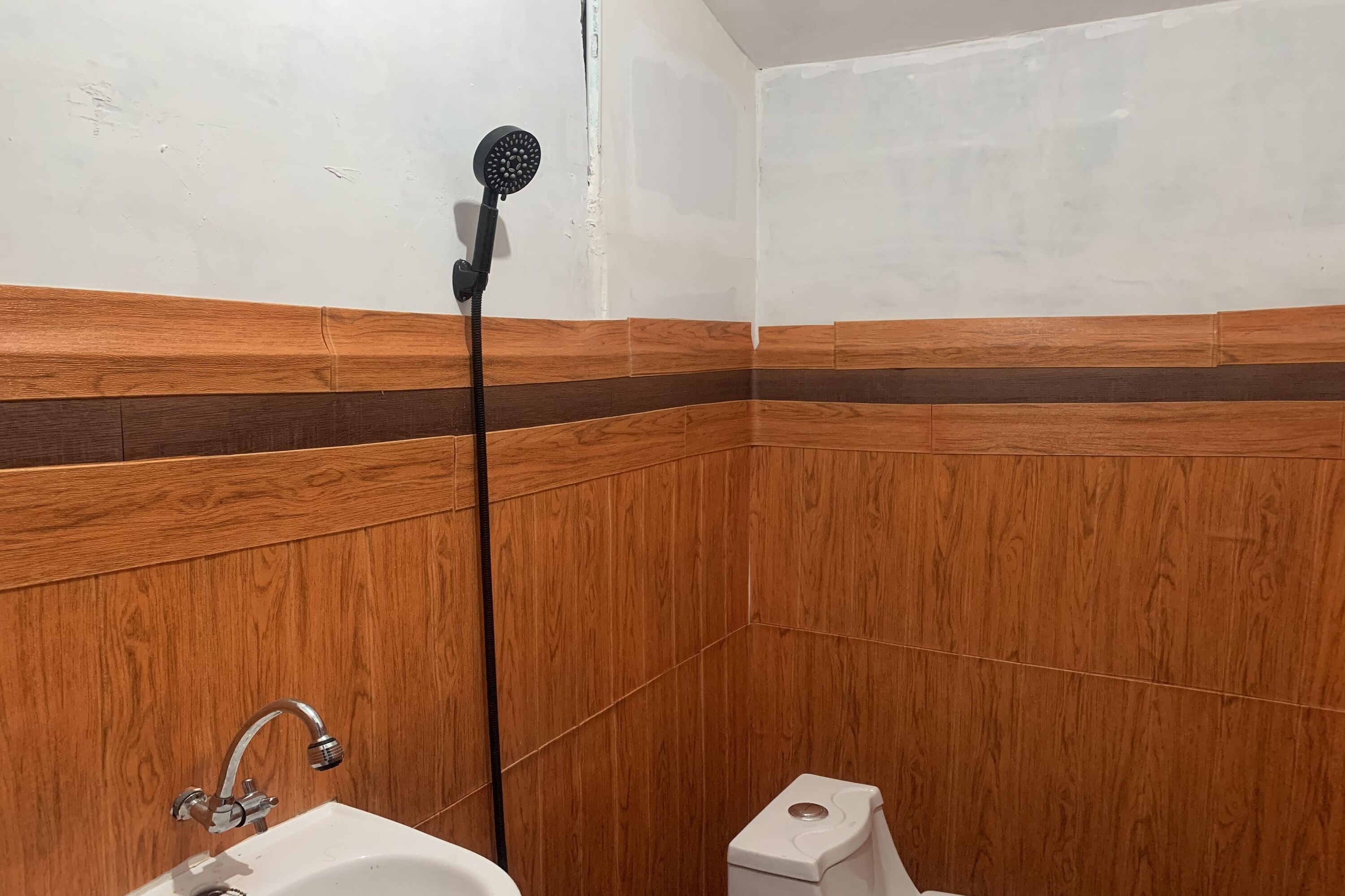 Un baño con paneles de madera, un lavamanos blanco y un cabezal de ducha.
