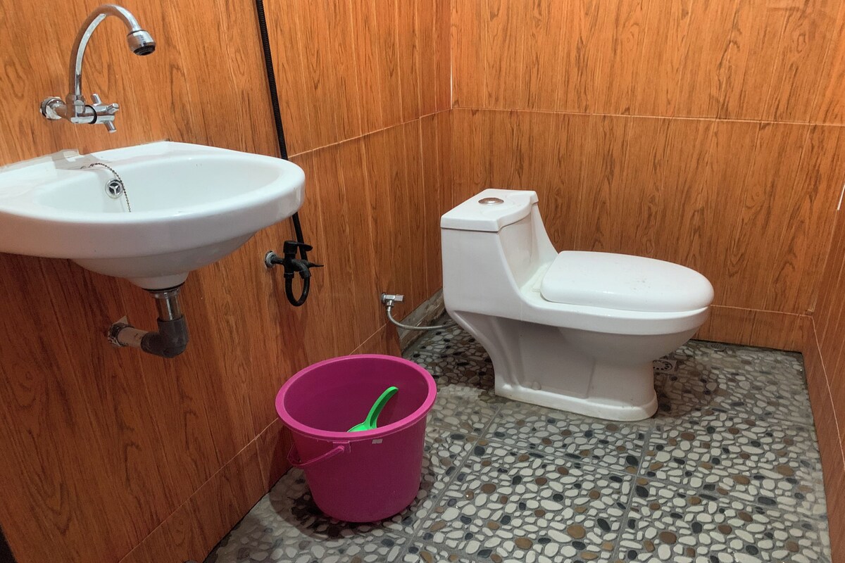 A bathroom with a white sink, a toilet, and a pink bucket on a tiled floor.