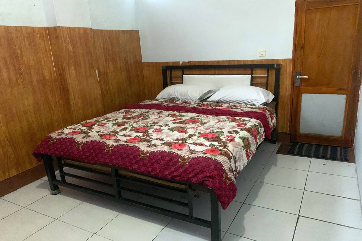 A bedroom with a wooden bed frame, a floral bedspread, and a red blanket.