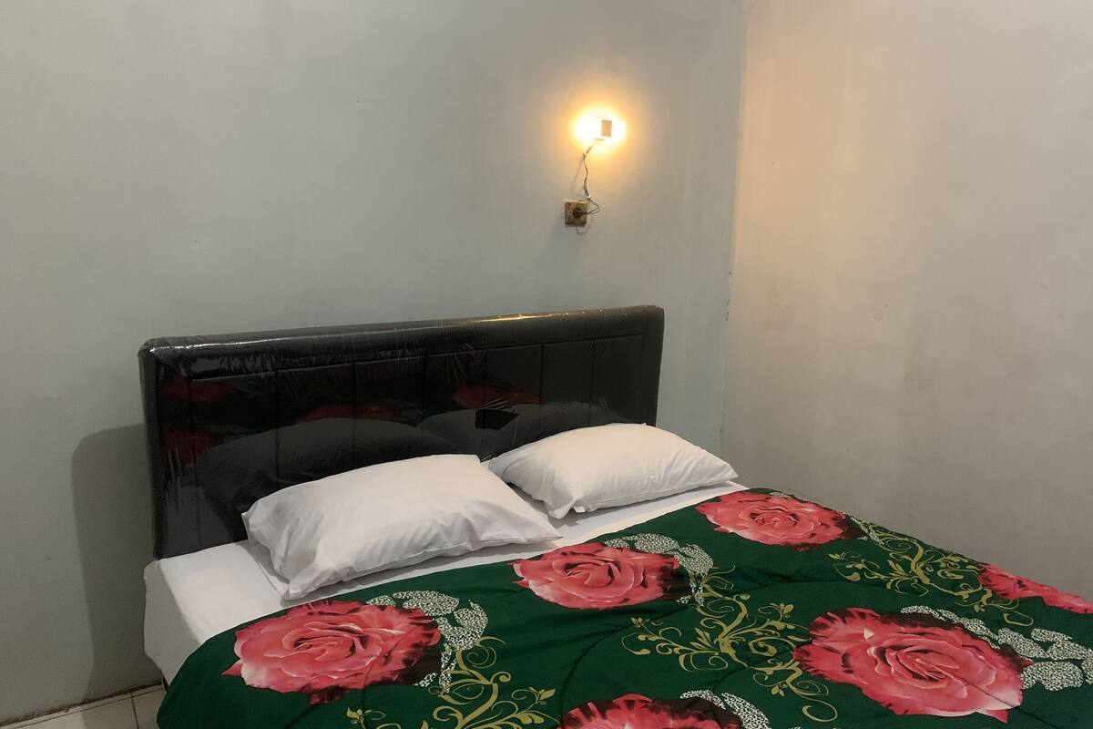 A bed with a floral bedspread, a headboard, and a wall-mounted light fixture.