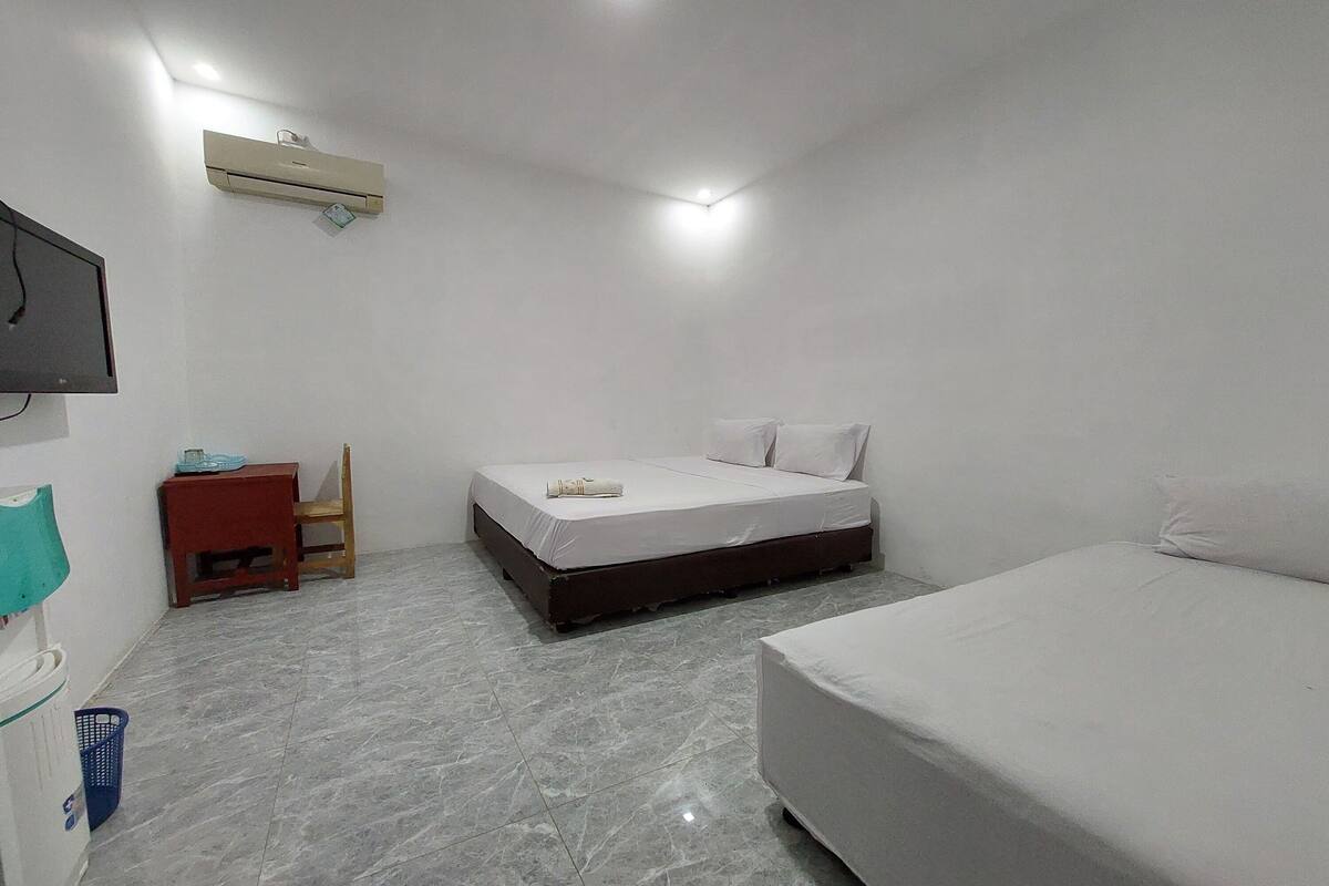 A room with a bed, a small table, a chair, an air conditioner, and a television mounted on the wall.