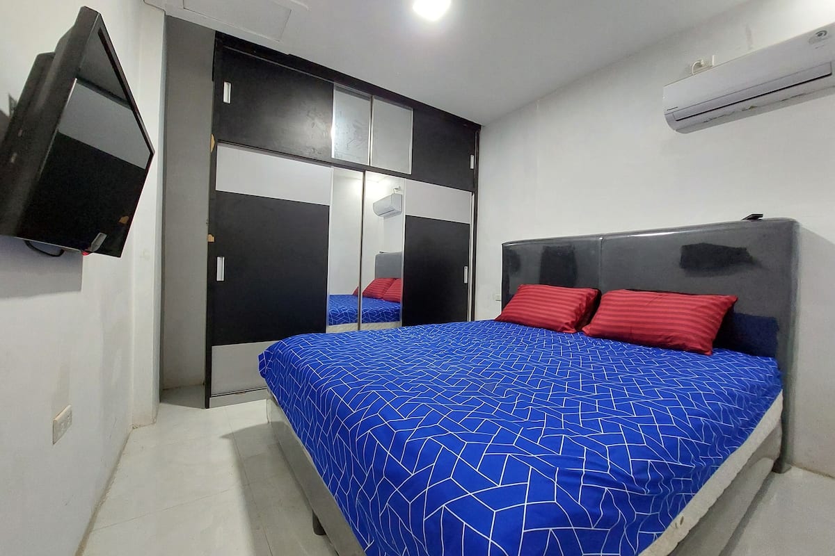 A bedroom with a bed, a wardrobe, a television, and an air conditioner.