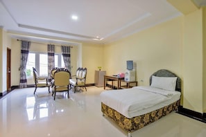 A hotel room with a bed, two chairs, a desk, a water dispenser, and a window with curtains. - Malibou Hotel Medan (Tebing Tinggi)