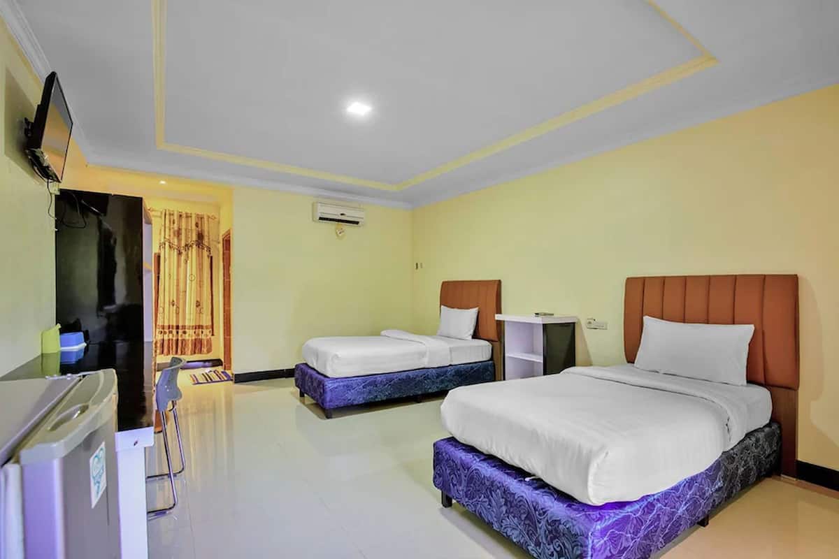 A hotel room with two beds, a TV, a desk, and a refrigerator.