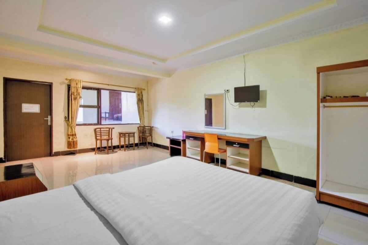 A hotel room with a bed, desk, chairs, a TV, and a wardrobe.