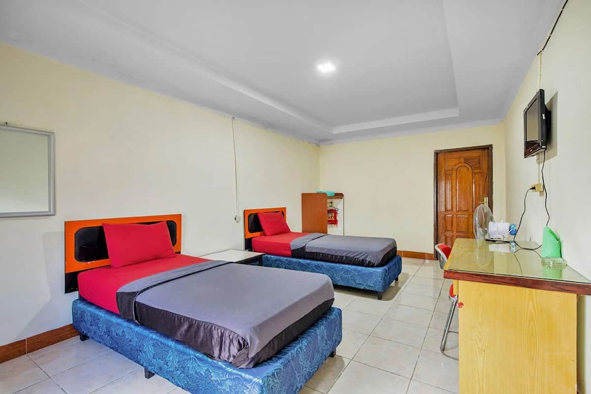A hotel room with two beds, a wooden desk, a television, and a door.
