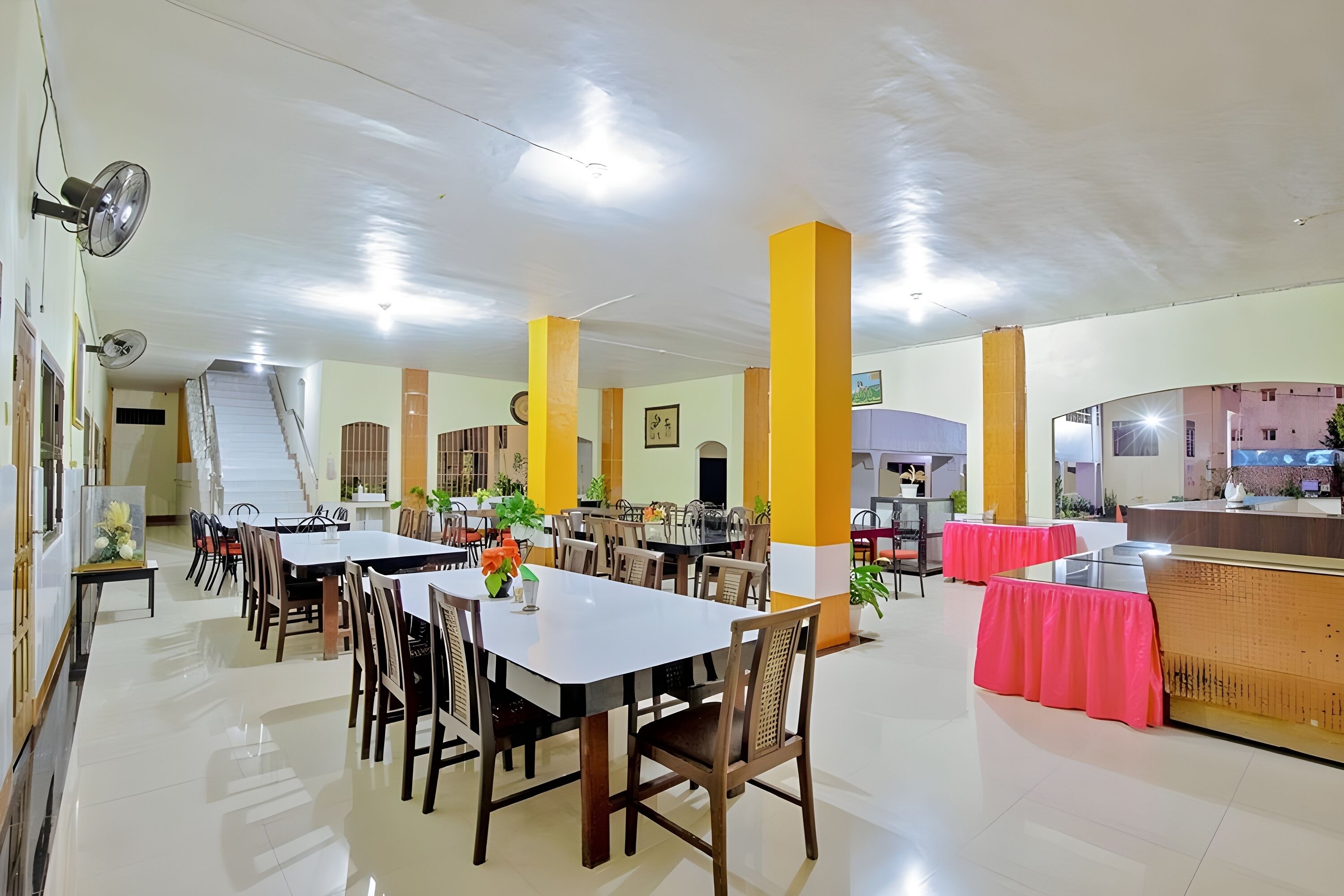 A spacious dining area with multiple tables and chairs, a reception desk, and a staircase leading to an upper level.