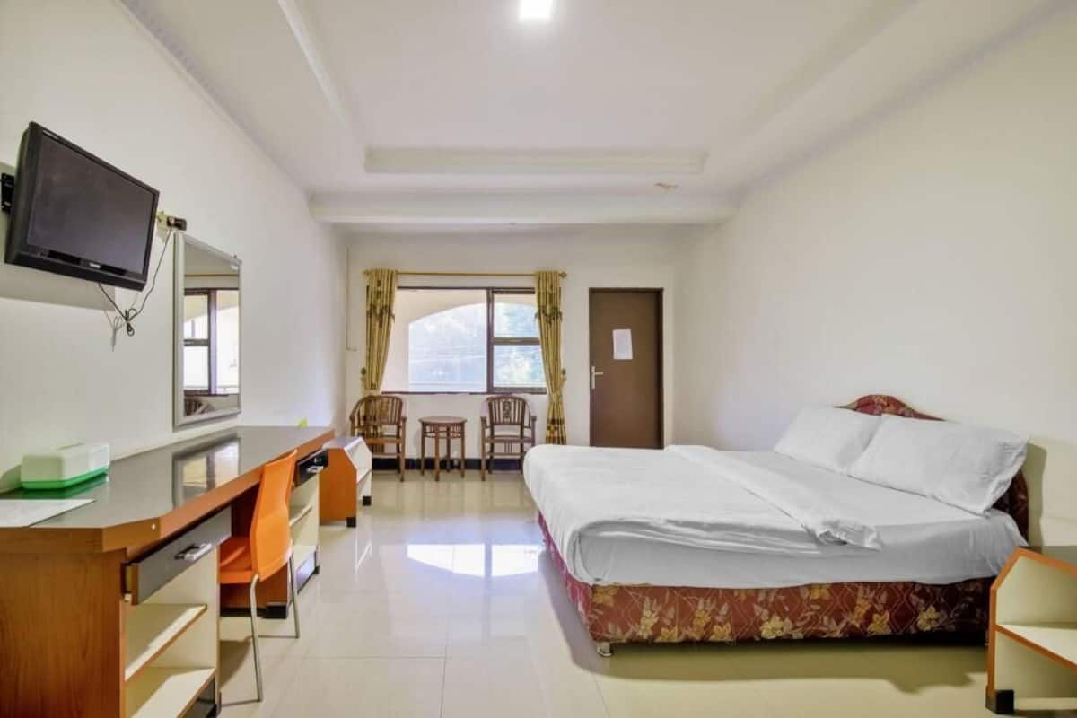 A hotel room with a bed, desk, chair, TV, and a window with curtains.