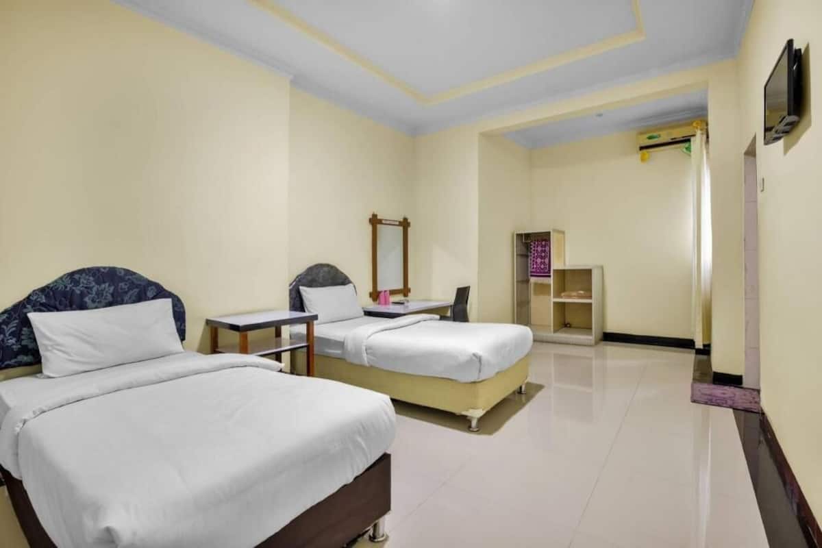 A hotel room with two beds, a desk, a chair, a TV, and a wardrobe.