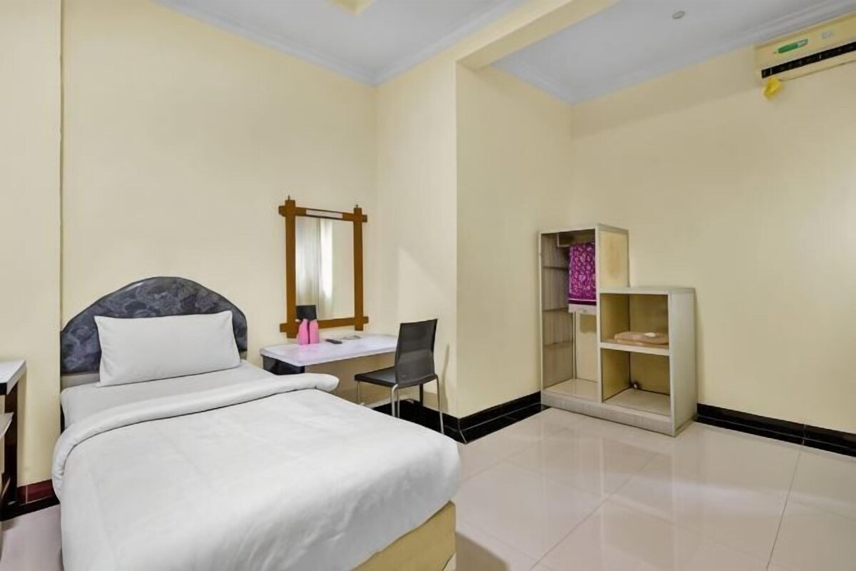 Een hotelkamer met een bed, een bureau, een stoel, een spiegel en een klein wandrek.