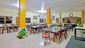 Un comedor amplio con varias mesas y sillas, un reloj en la pared y plantas en macetas.