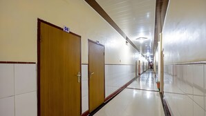 Un largo pasillo bien iluminado con puertas de madera y paredes de baldosas blancas.