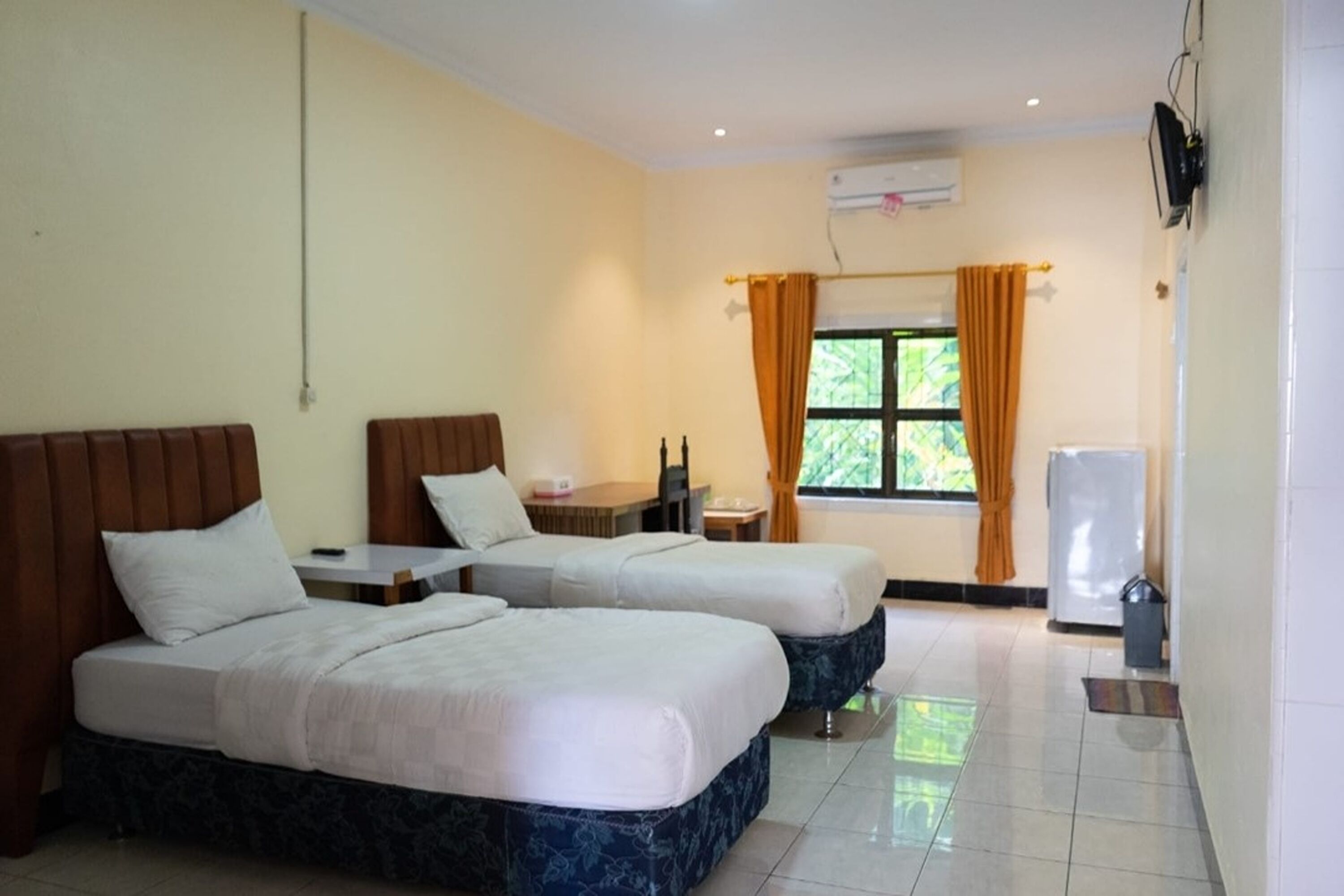 A hotel room with two beds, a small table, a TV, and a window with curtains.
