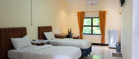 A hotel room with two beds, a small table, a TV, and a window with curtains.