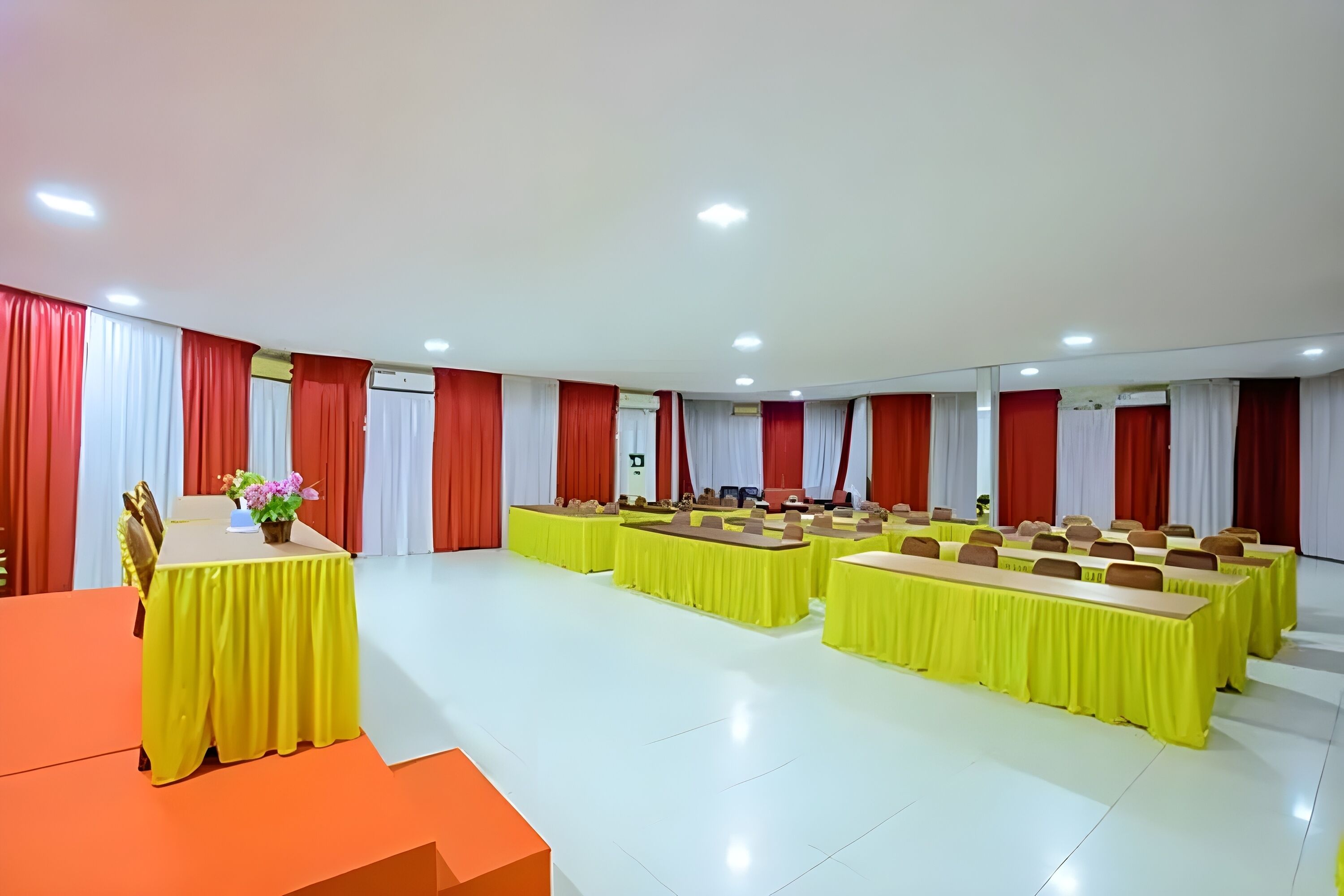 A conference room with multiple tables, red and white curtains, and a podium with a flower arrangement.