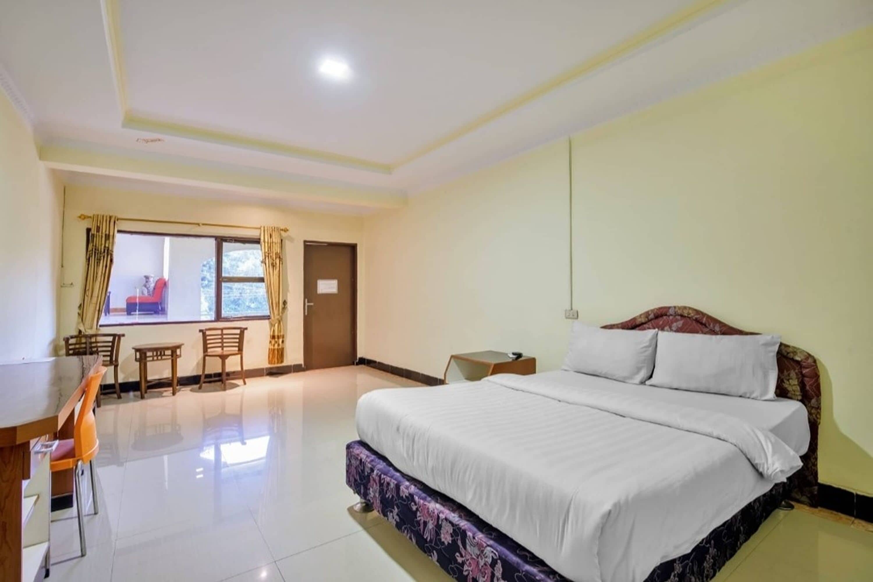 A hotel room with a bed, a desk, chairs, and a window with curtains.
