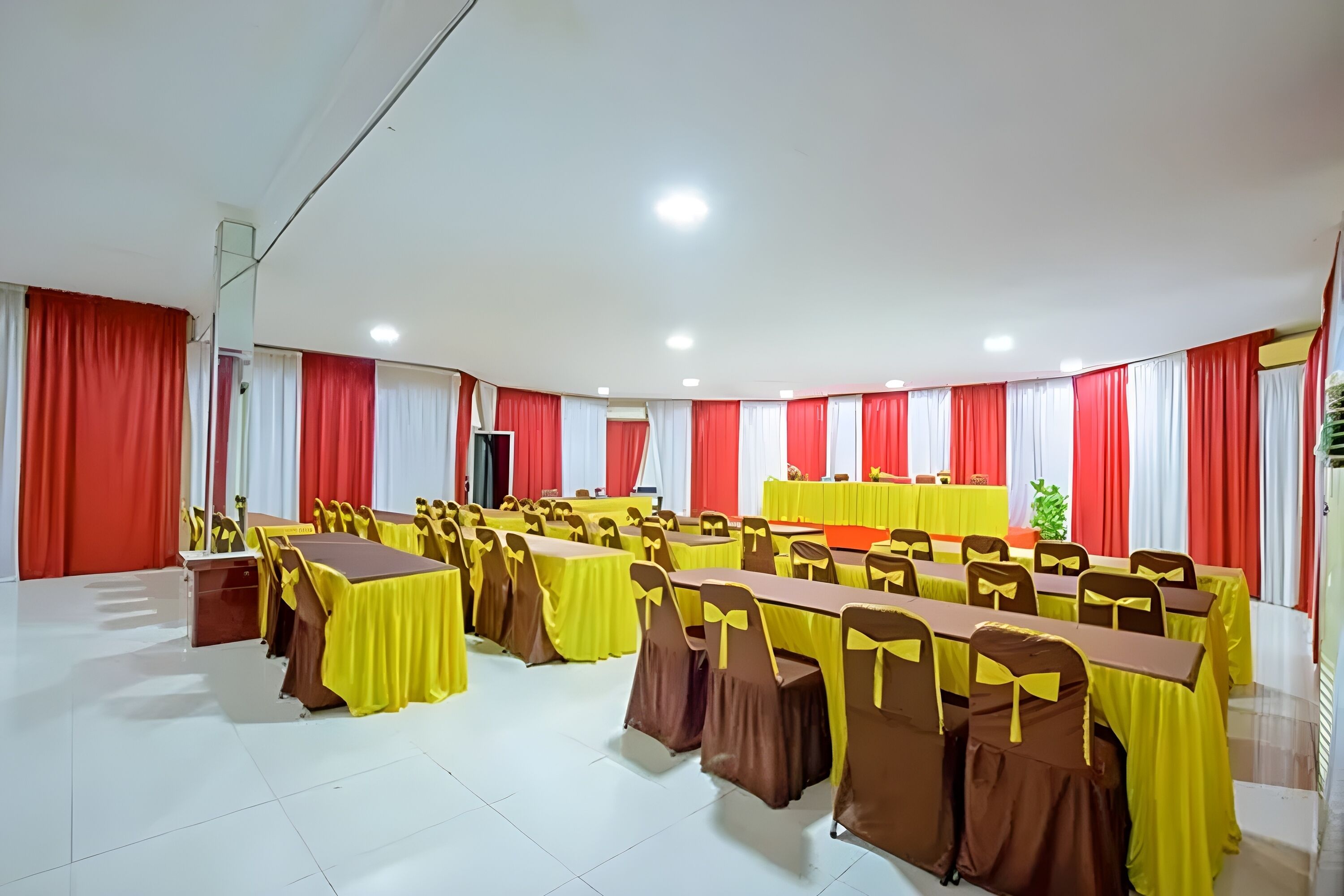 A conference room with multiple tables and chairs, red and white curtains, and a podium.