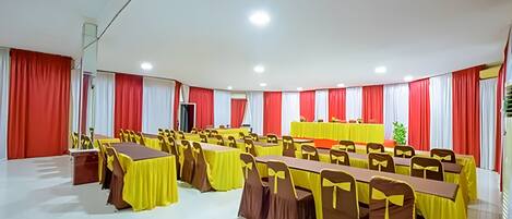 A conference room with multiple tables and chairs, red and white curtains, and a podium.