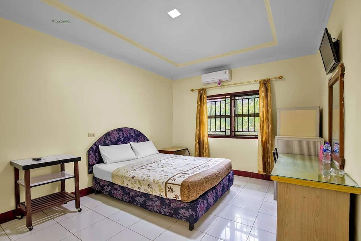 A bedroom with a bed, a bedside table, a desk, a window with curtains, and a radiator.