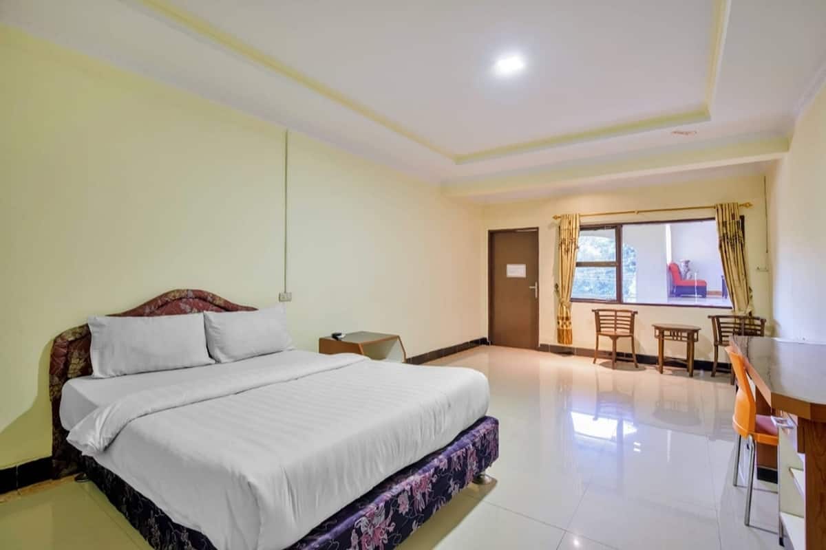 A hotel room with a bed, a small table, and a window with curtains.