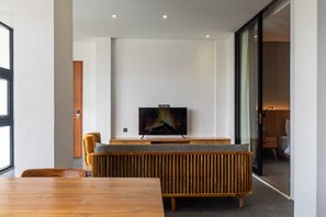 A modern living room with a wooden dining table, a comfortable sofa, and a flat-screen TV mounted on the wall.