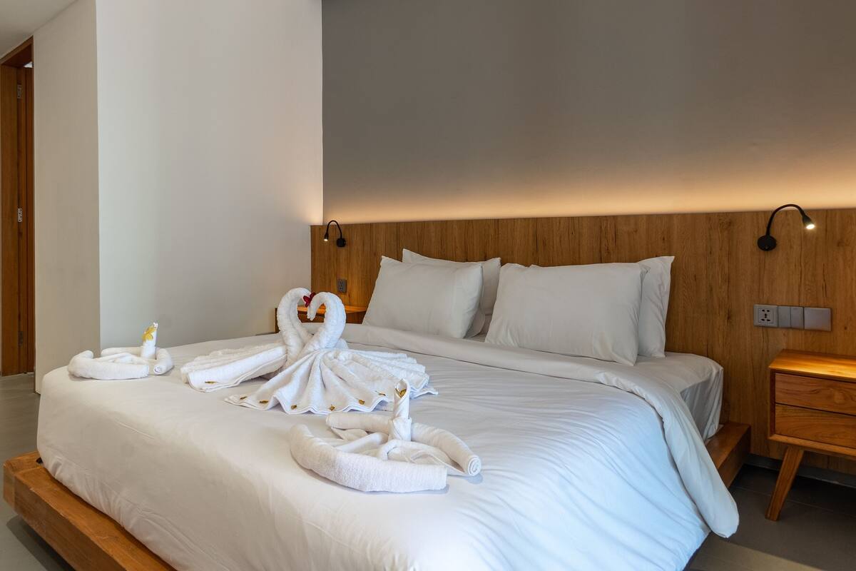 A neatly made bed with white linens and a swan-shaped towel arrangement.