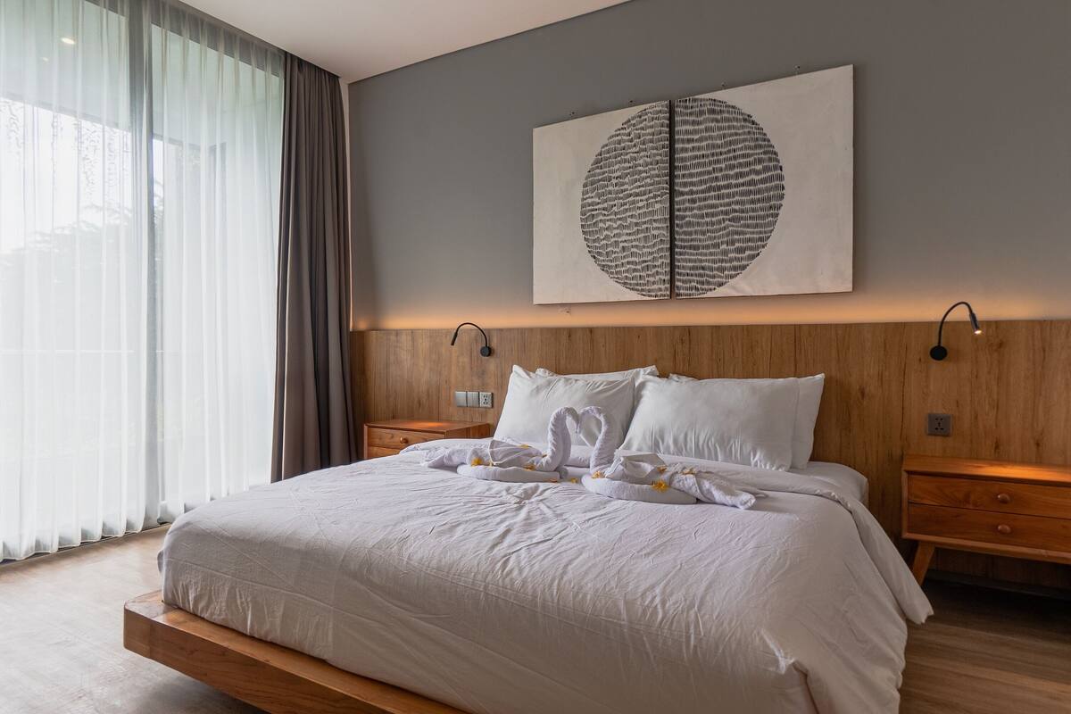 A modern hotel room with a large bed, wooden headboard, and a wall-mounted artwork.
