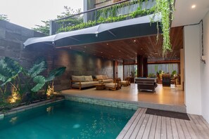A modern indoor pool area with a wooden deck, lounge seating, and a pool table.